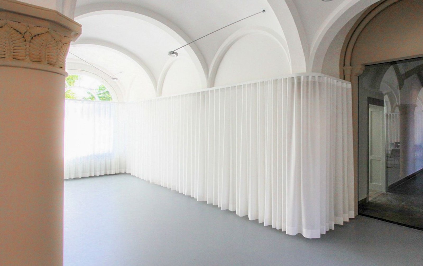 White curtains following a curved ceiling track beneath vaulted arches