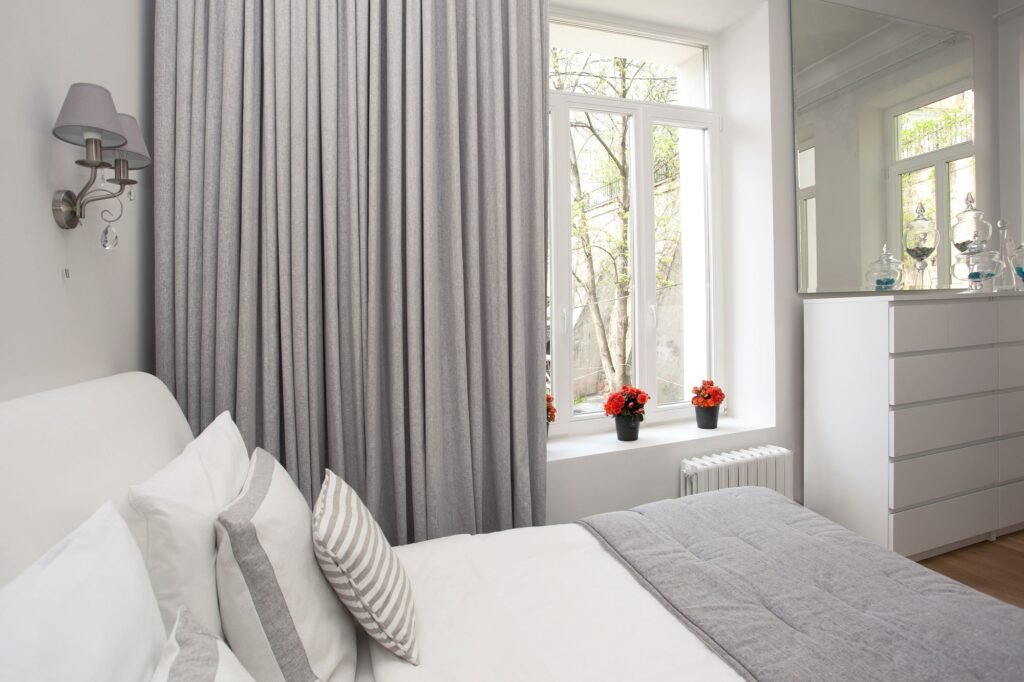 Grey drapes beside a window in a calm white bedroom
