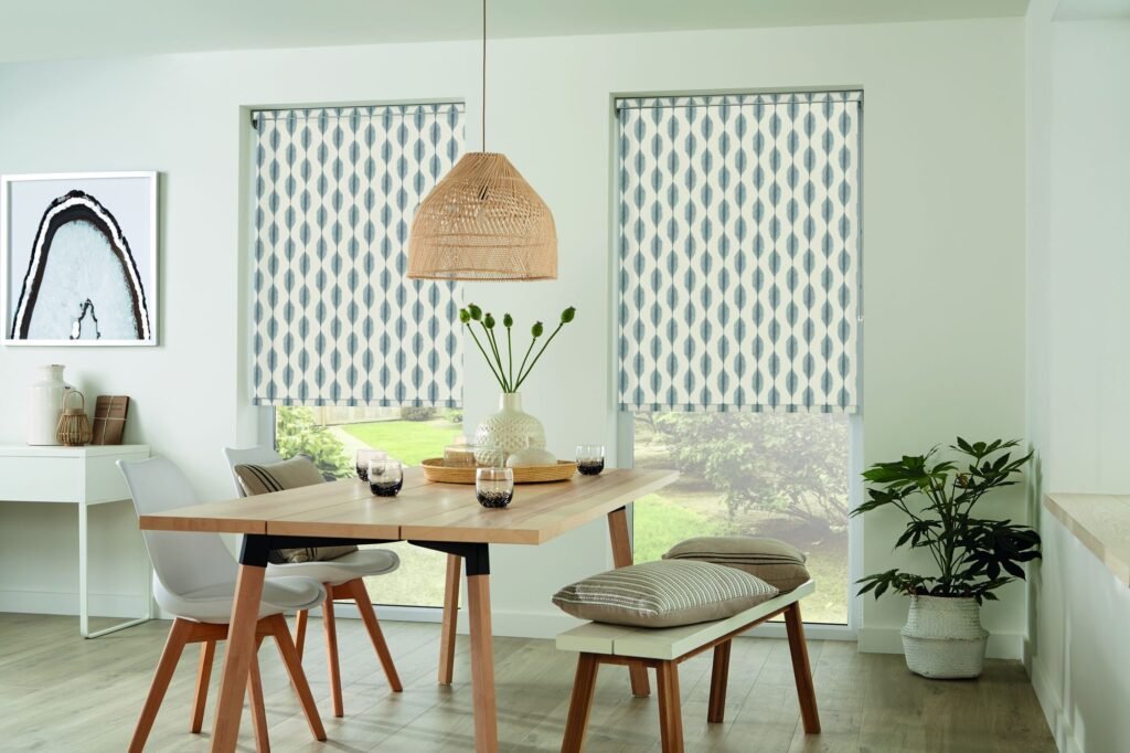 Patterned roller blinds above a timber dining table in a pale green room