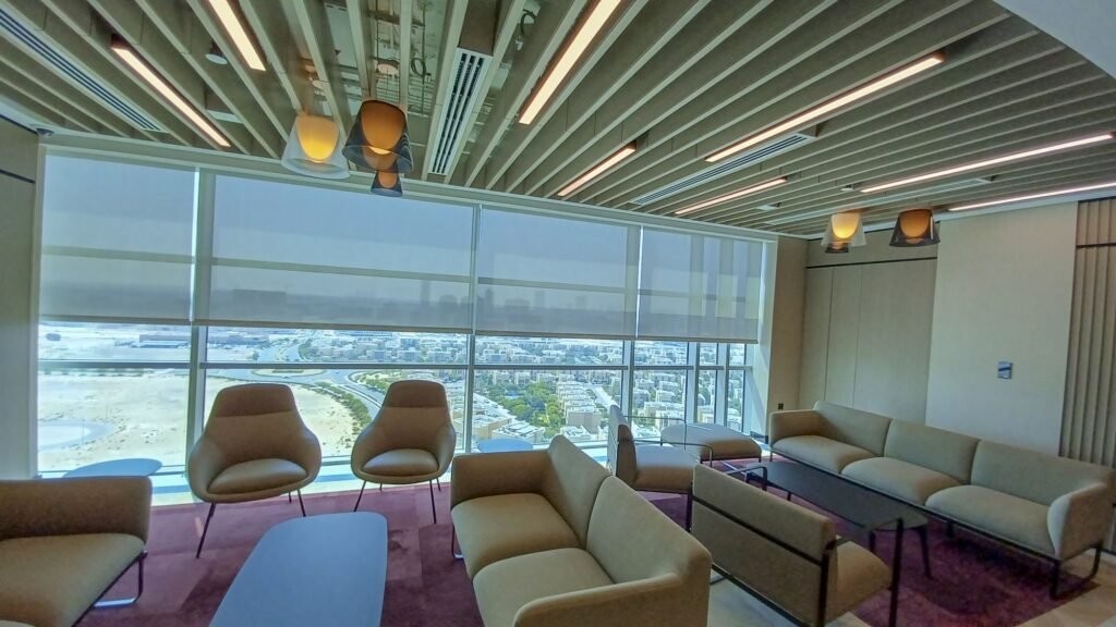 Light-filtering roller blinds lowered across a wall of glazing in a lounge with a city view