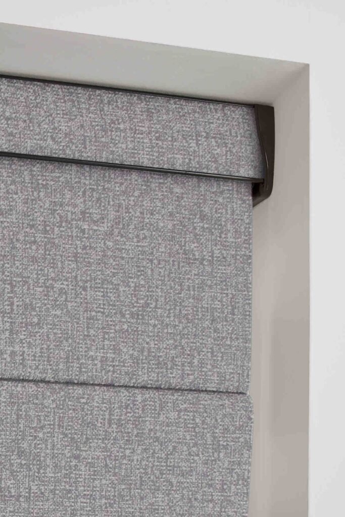 Close view of the stacked fabric folds of a grey Roman blind
