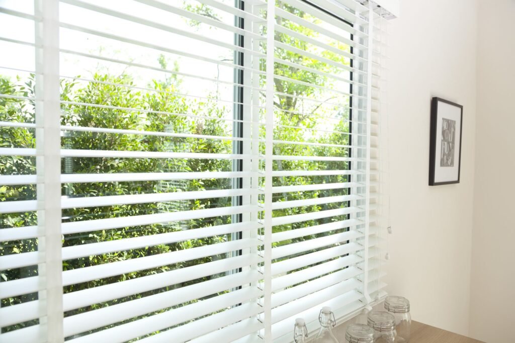 White Venetian blind with slats tilted open to a green garden