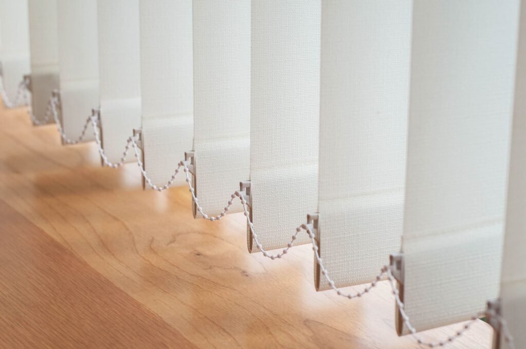 Close view of white vertical louvres joined by a bottom chain