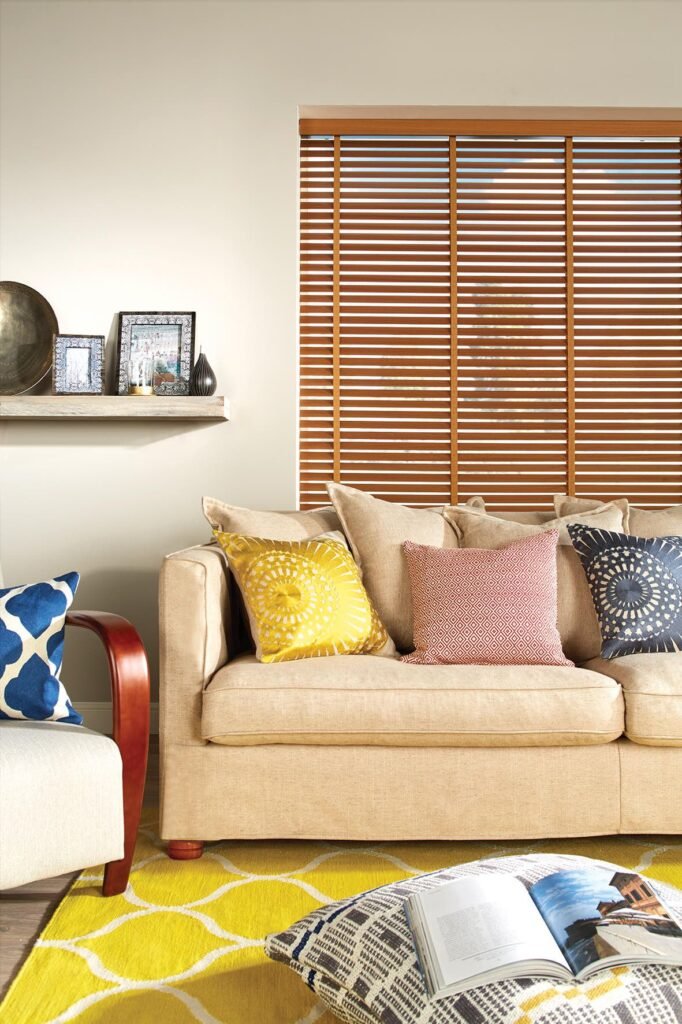 Wooden blind on a tall window behind a sofa with yellow cushions